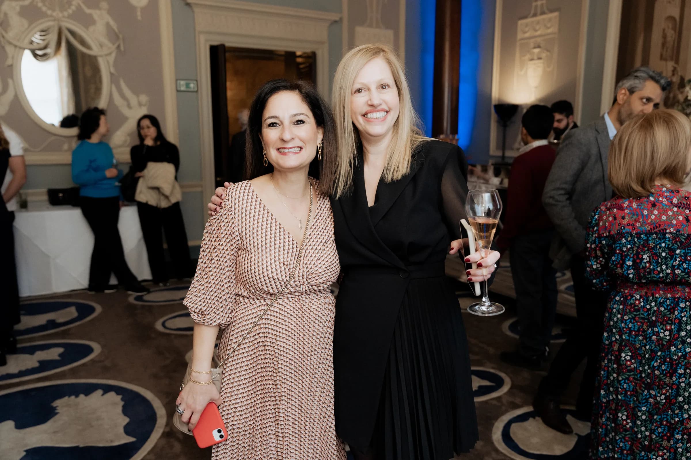 Two guests smiling with a glass of champagne in a Wedgwood-blue hotel ballroom with plaster reliefs and blue uplighting in London