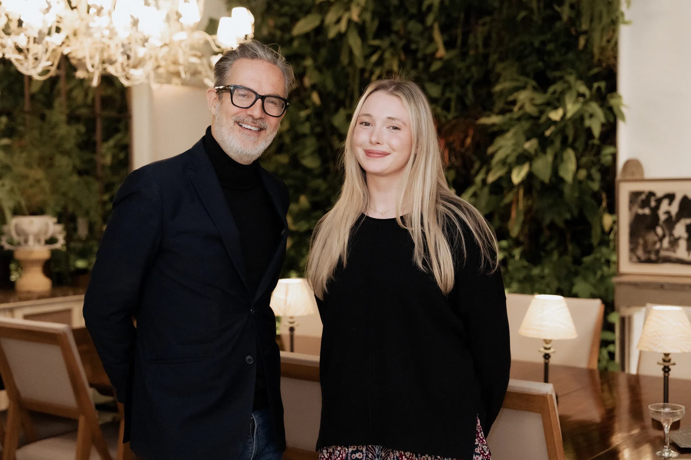 Les hôtes Hometainment en tablier vert avec des invités devant un mur végétal sous un lustre, lors d'une soirée dans un showroom londonien