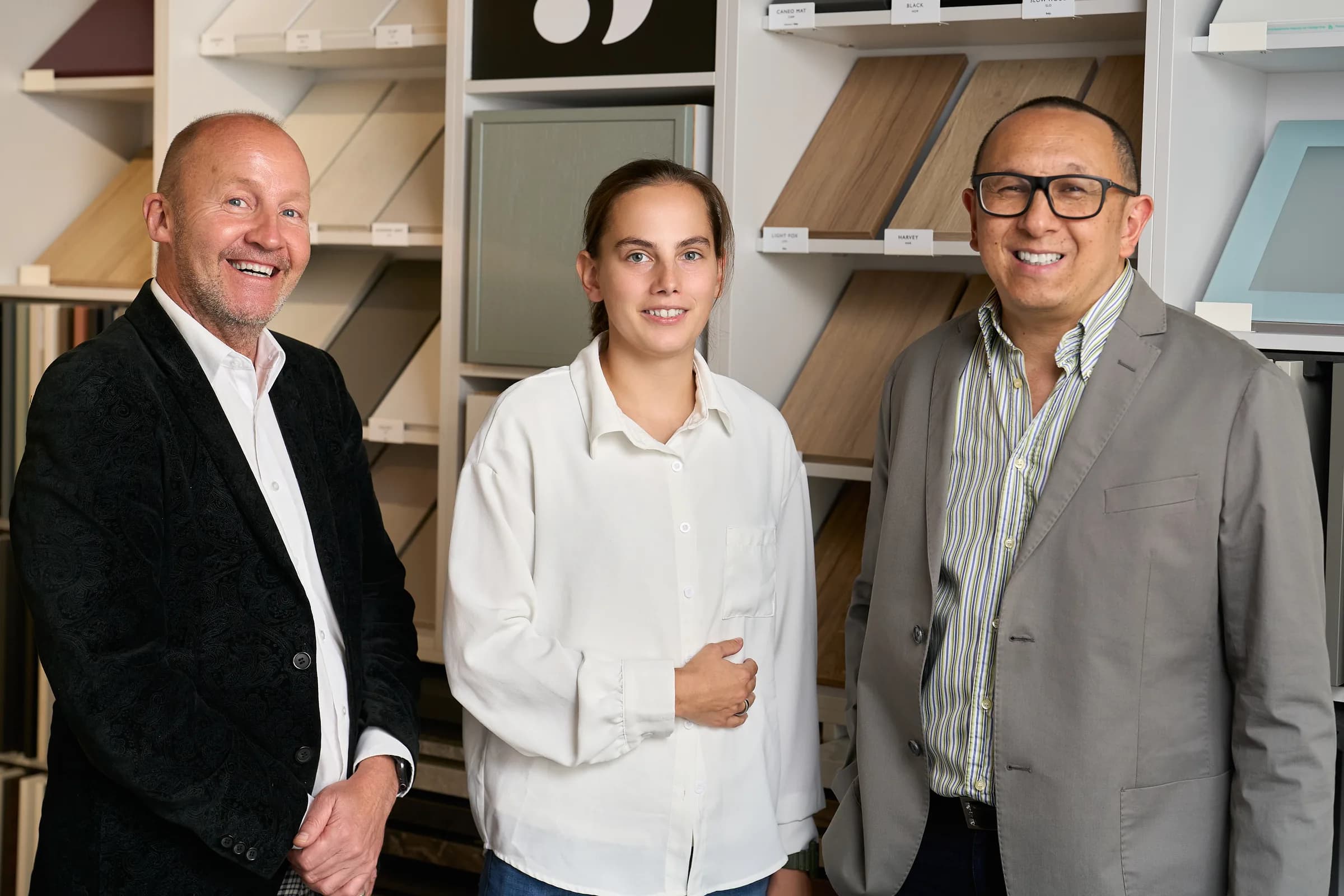 Trois membres de l'équipe du showroom Schmidt d'Islington souriant devant un mur d'échantillons de façades en bois et en laque