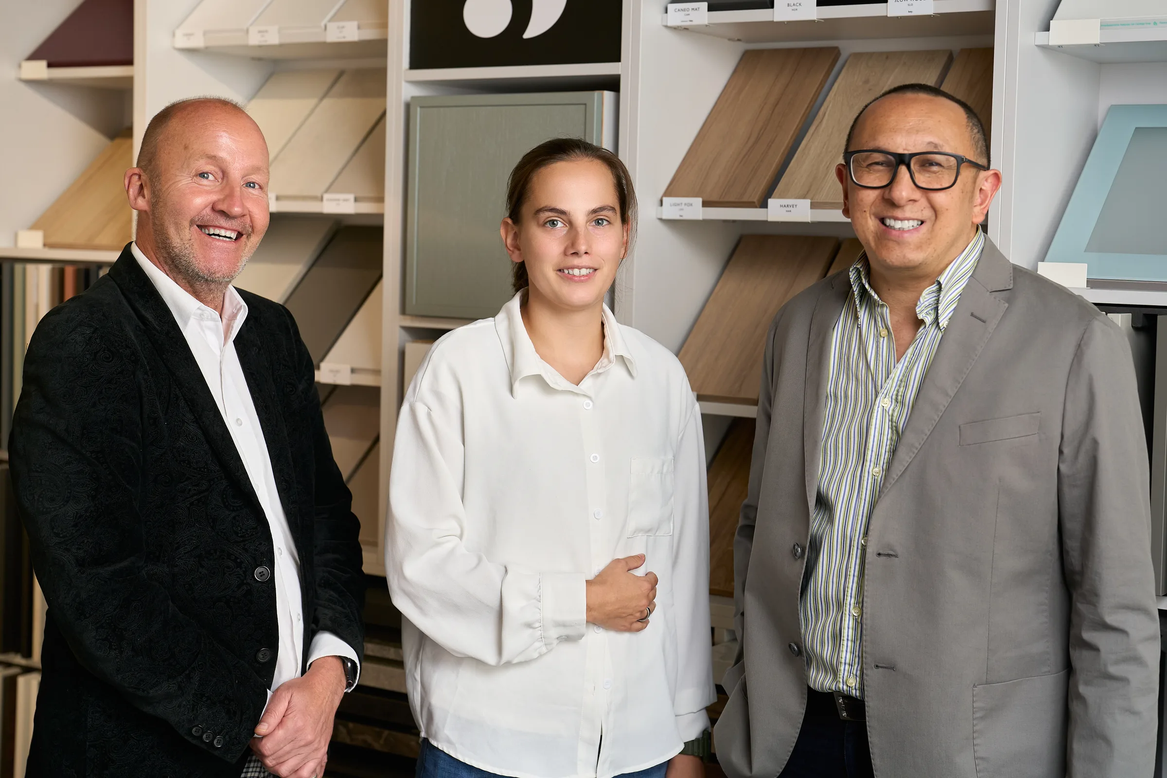 Trois membres de l'équipe du showroom Schmidt d'Islington souriant devant un mur d'échantillons de façades en bois et en laque