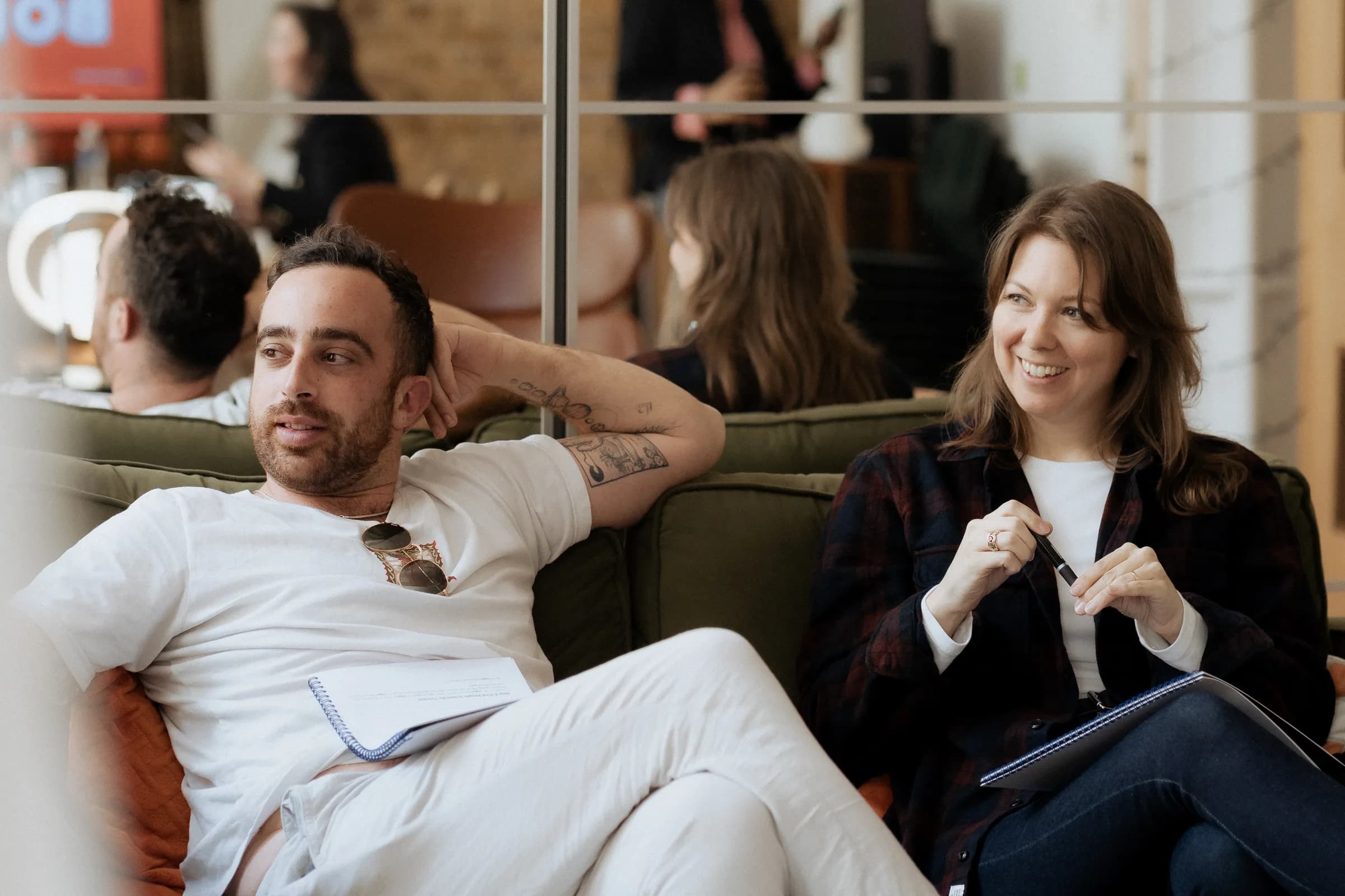 Workshop participants writing at a table under a screen reading BONJOUR BONJOUR in a brick-walled London loft