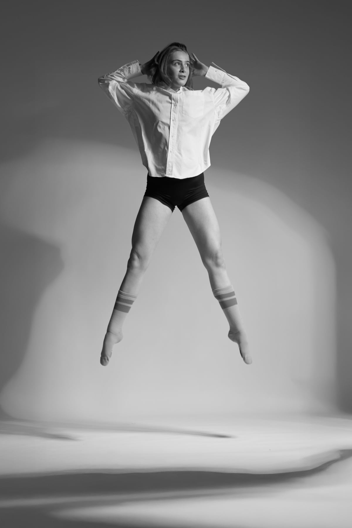 Black-and-white artistic portrait of a contemporary dancer holding a sculptural pose in a London studio, lit with high-contrast directional light