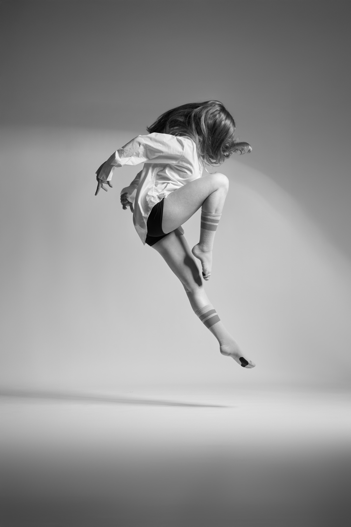Black-and-white artistic portrait of a contemporary dancer holding a sculptural pose in a London studio, lit with high-contrast directional light